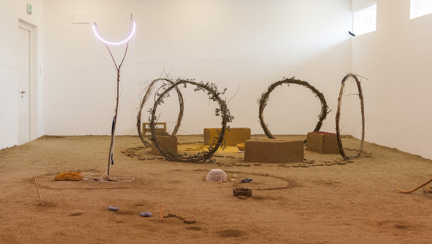 Lerato le le golo (...la go hloka bo kantle), 2022, Branch with blue ribbon, neon light, rock, clay lid with herbs, 3 soaps (dinosaur, crocodile, turtle), 4 soil cubes, 4 circles made of branches, herbs, clay bowl, dimensions variable