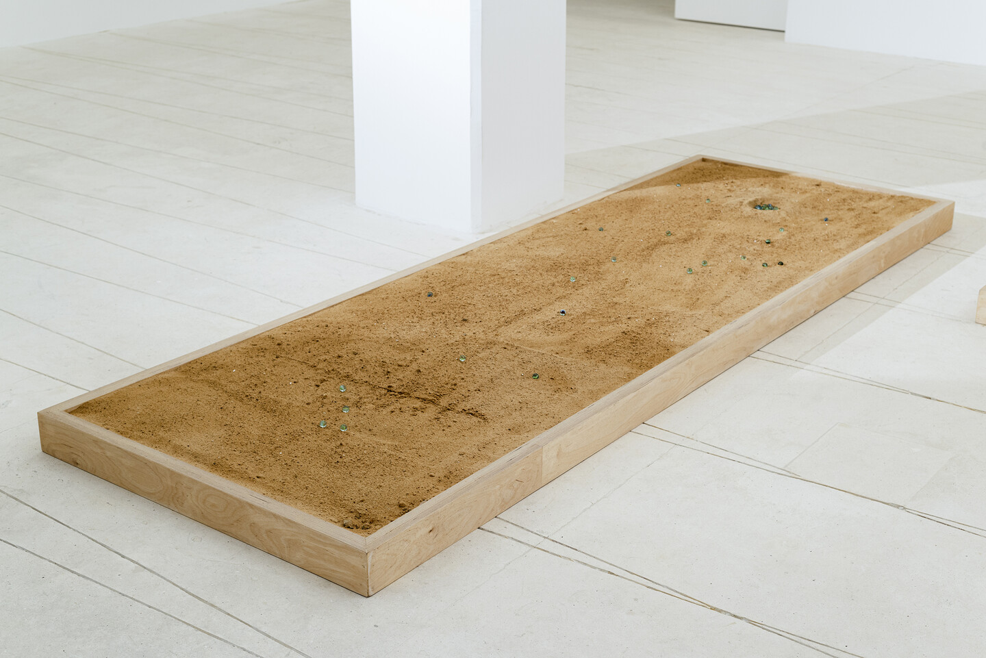 Marbles, 2024, 7 heated glass marbles, sand, wood, 300 &times; 100 &times; 10 cm